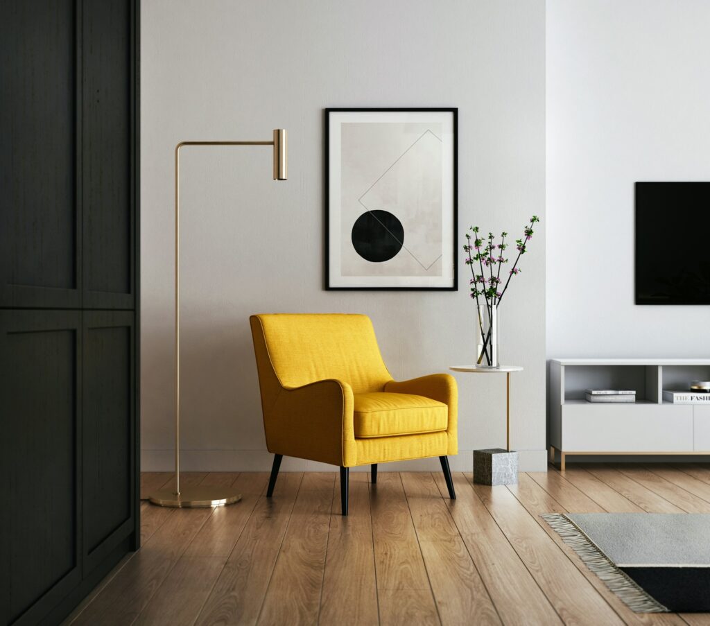 A yellow chair in a living area. There’s also a modern brass lamp and geometric art on the wall. Home staging requires an eye for design just as much as keen business sense.