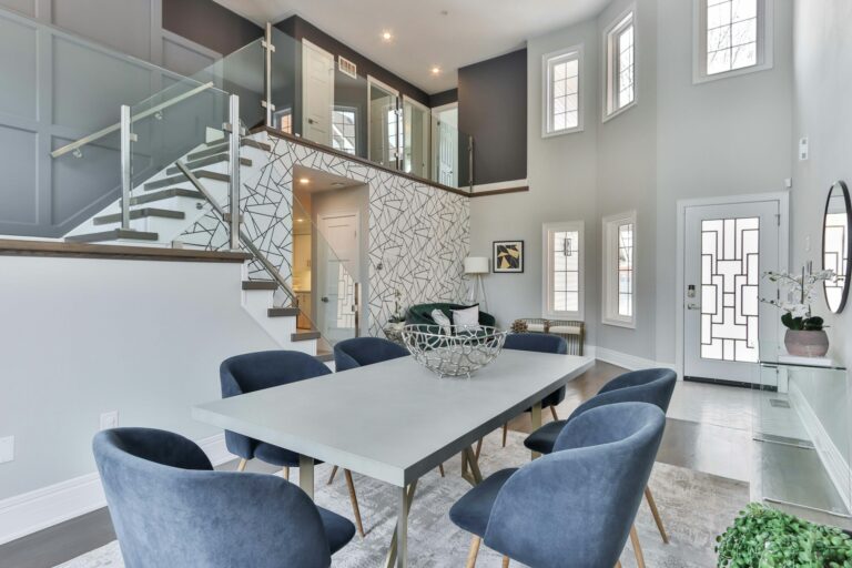 A luxury dining space inside a home with a white table and blue cloth-covered chairs.